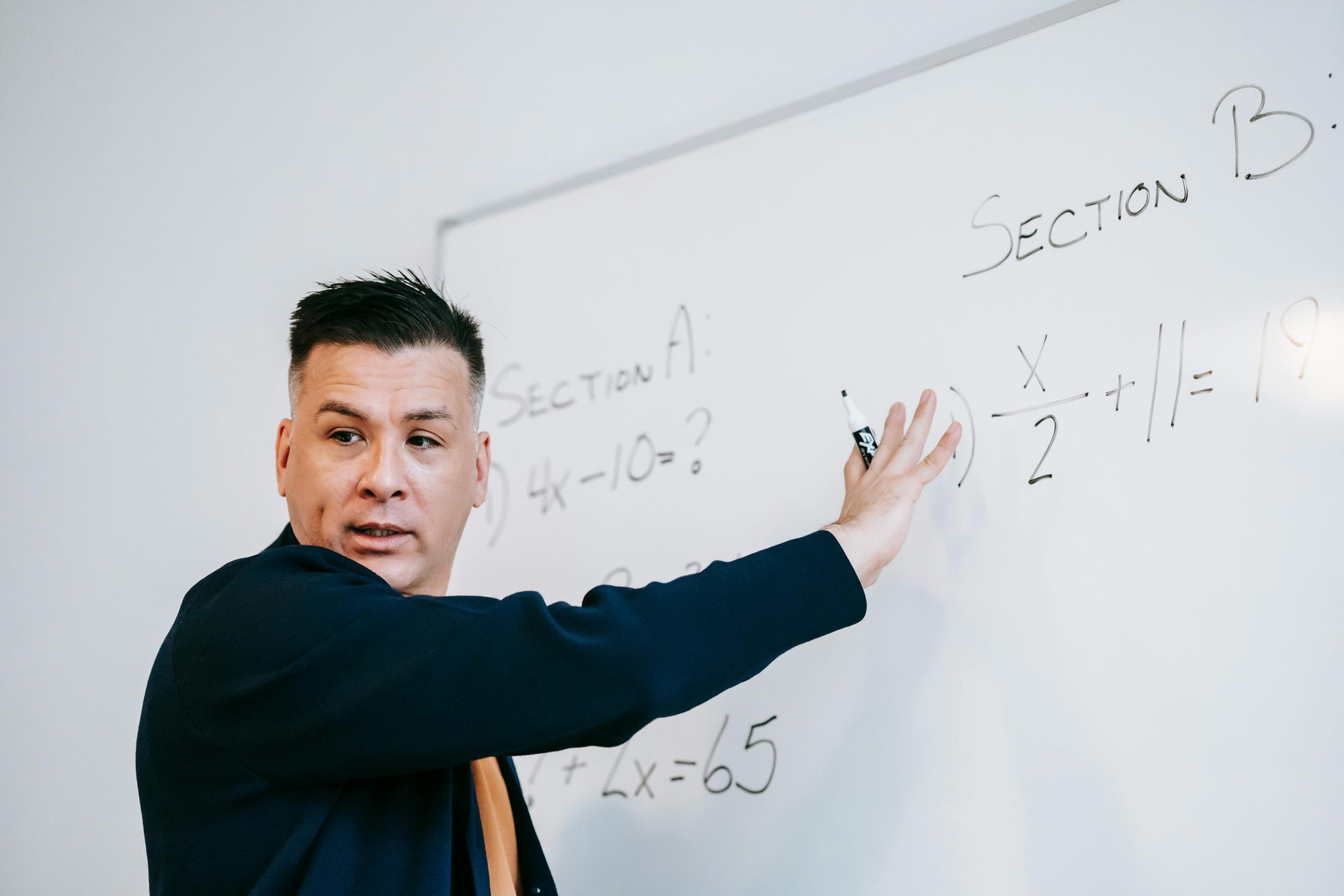 Educator in a structured setting explains algebraic equations on a whiteboard.