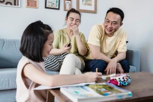 A happy family sitting together in the living room while a child focuses on homework.